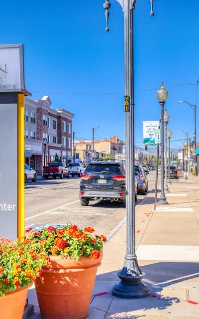 A view of a city street with a signpost indicating various locations such as the Post Office, RTD Light Rail Station, Arapahoe Community College, and Littleton Center. Colorful flower pots are in the foreground and shops line the street.