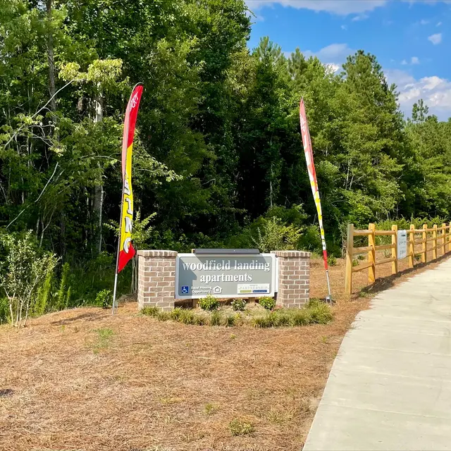 Sign for Woodfield Landing next to a pathway with greenery and trees in the background.