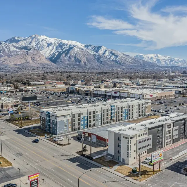 Aerial view of a city with a mountain backdrop, showcasing commercial buildings and roads.