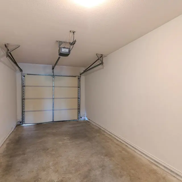A spacious, empty garage with concrete flooring and white walls, featuring a garage door that is closed.