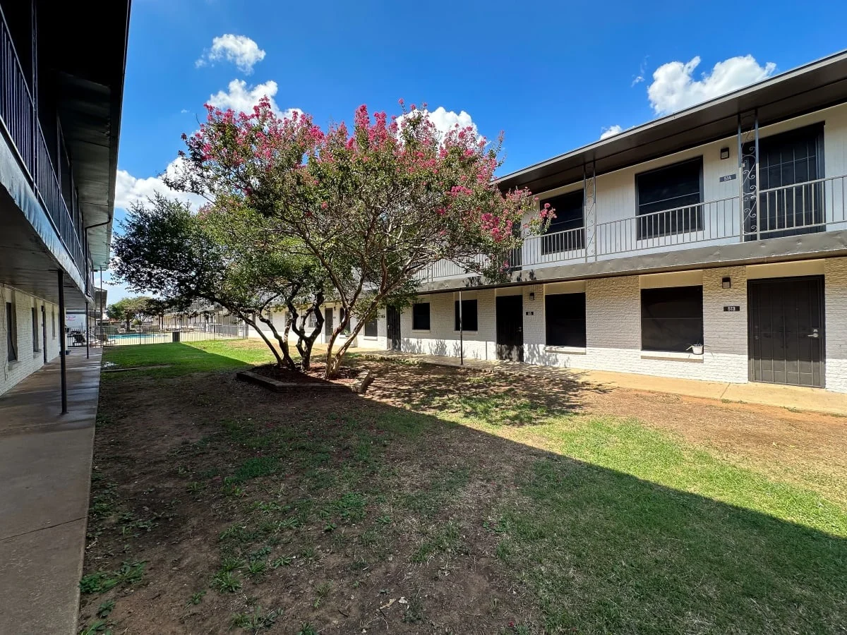 Apartment Complex Landscape View of an apartment complex with two-story buildings and a small lawn area featuring a flowering tree.