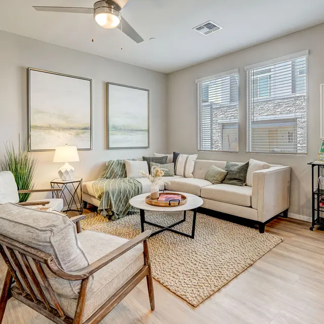 A cozy living room with a sectional sofa, armchairs, decorative art on the walls, and natural light from large windows.
