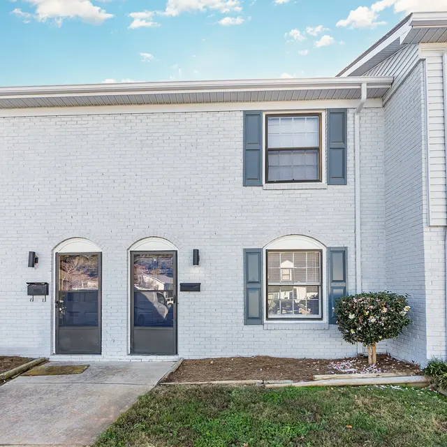 Exterior view of a townhouse with two doors and several windows, featuring white brick and blue shutters.