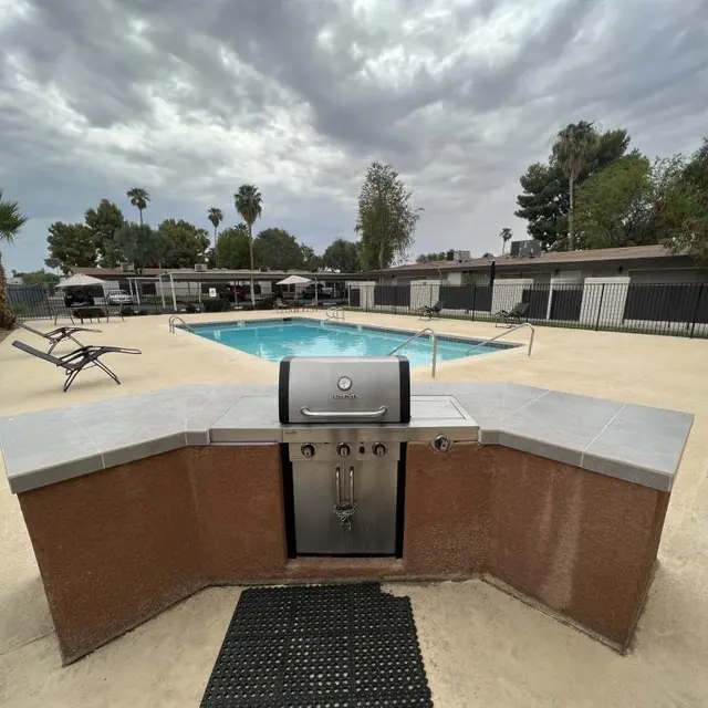 Barbecue Area by the Pool A barbecue grill area facing a pool with lounge chairs and cloudy skies in the background.