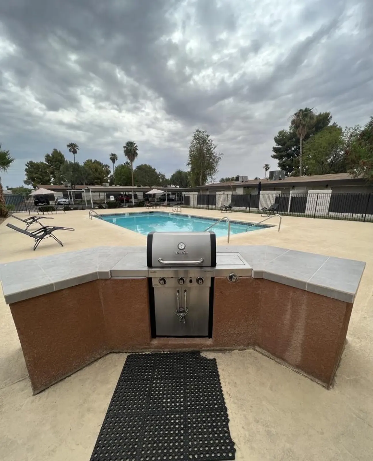 Grill station facing the pool and lounge chairs beneath a cloudy sky.