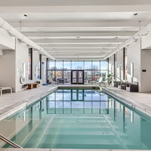 A spacious indoor swimming pool area with loungers and large windows letting in natural light.