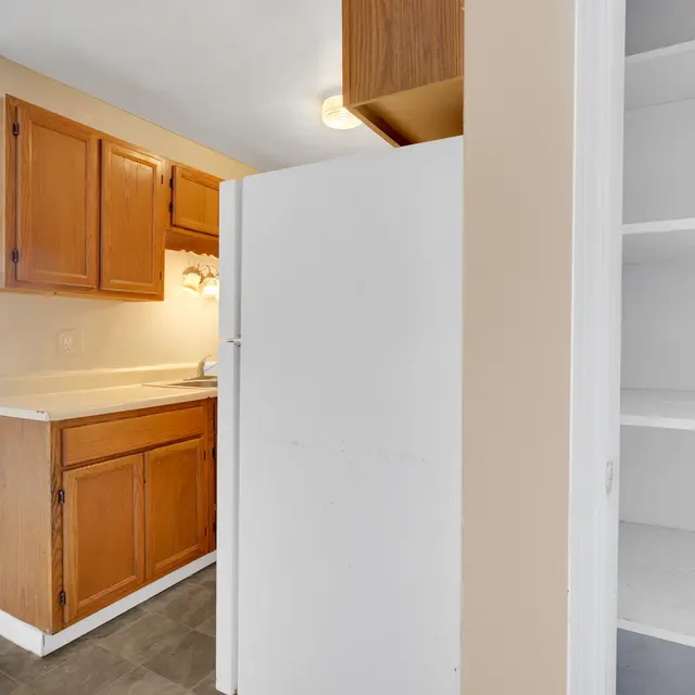View of a kitchen with wooden cabinets, a white refrigerator, and an empty pantry space.