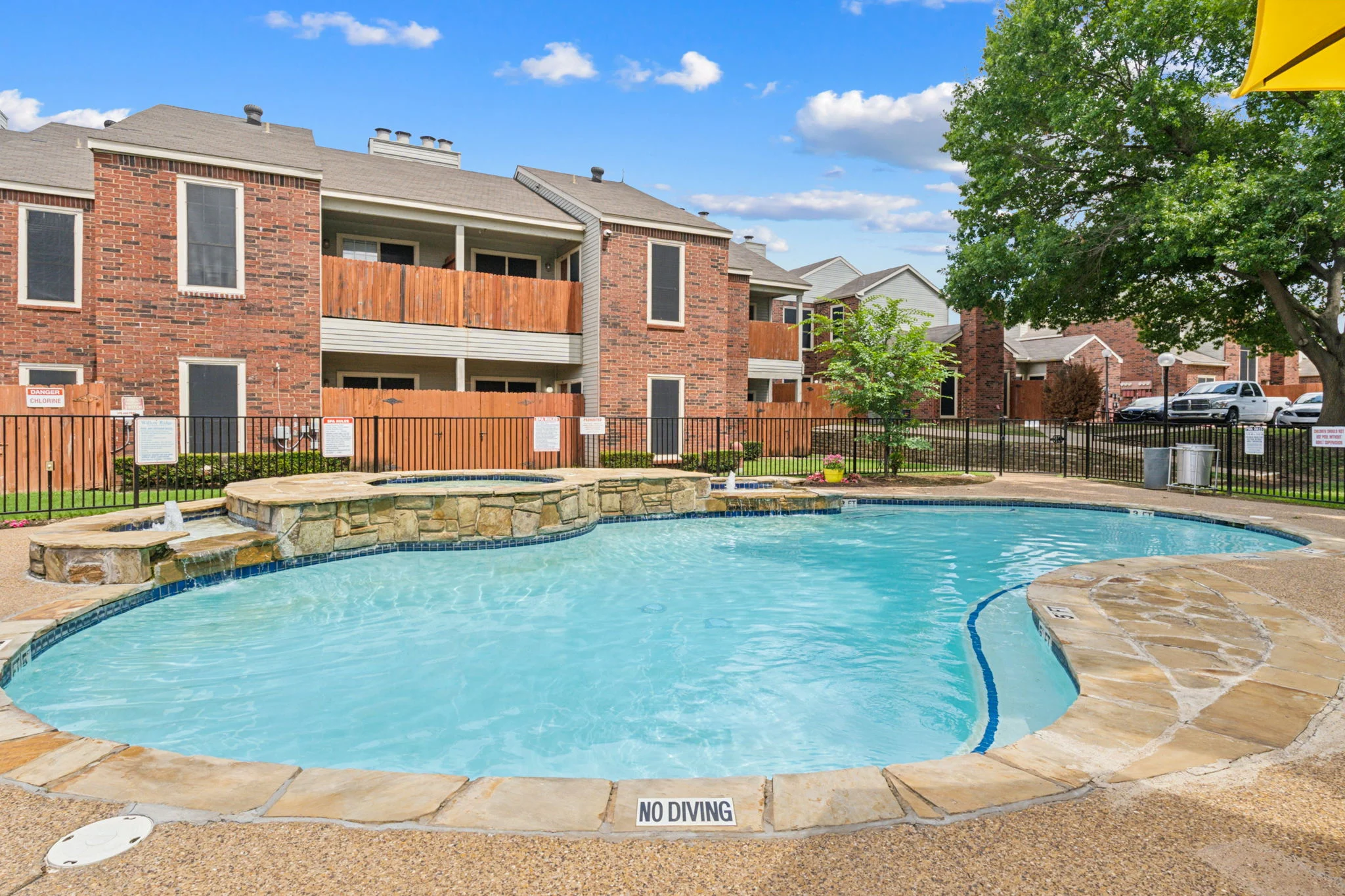 Swimming pool in an apartment complex surrounded by brick buildings and greenery.