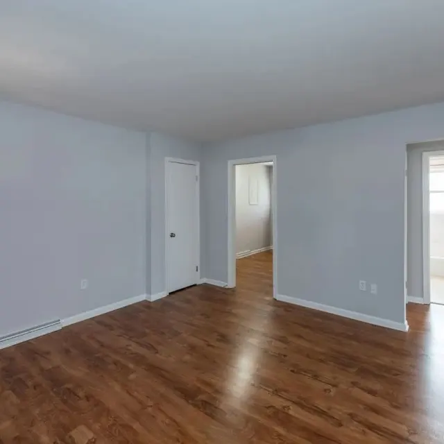 A spacious, empty room with gray walls and hardwood flooring. There are two doorways leading to other areas and ample natural light entering through the windows.
