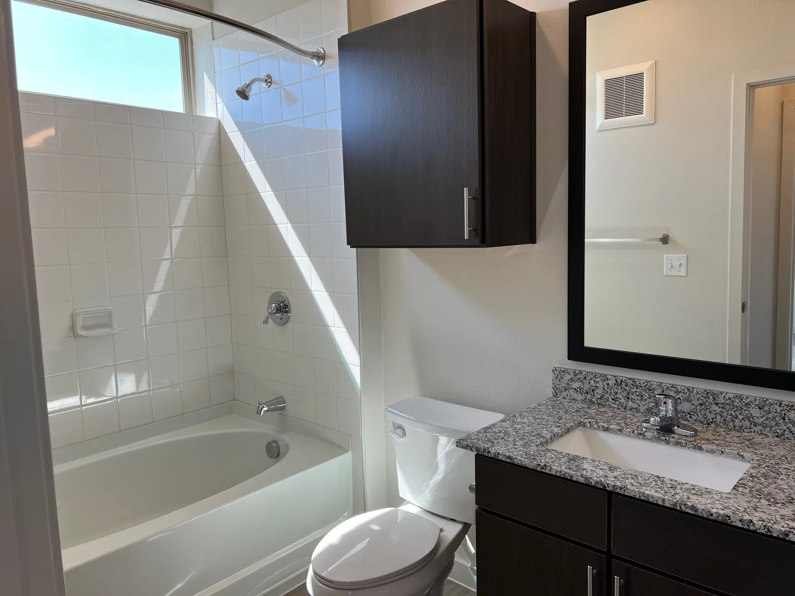 Modern Bathroom Design A well-lit modern bathroom featuring a shower-tub combo, granite countertop washbasin, and dark wood cabinetry.
