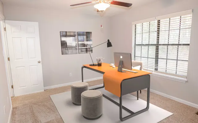 Summit at 501 Modern office space featuring a sleek desk with an orange runner, two stools, a computer, and a ceiling fan by a window.