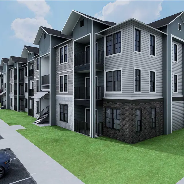 Three-story residential building with a mix of gray and black accents, surrounded by greenery and parked cars.