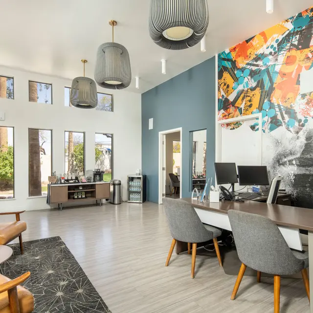 Modern office space featuring a colorful mural, large windows, stylish furniture, and a clean, bright aesthetic.