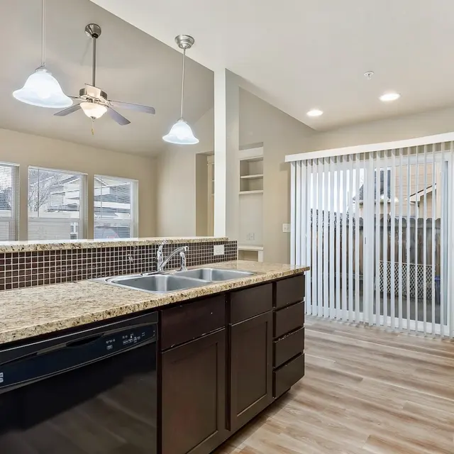 Bowery Point A modern kitchen with dark cabinets, granite countertops, stainless steel appliances, and a sliding door to an outdoor patio. The space features three pendant lights and a dishwasher.