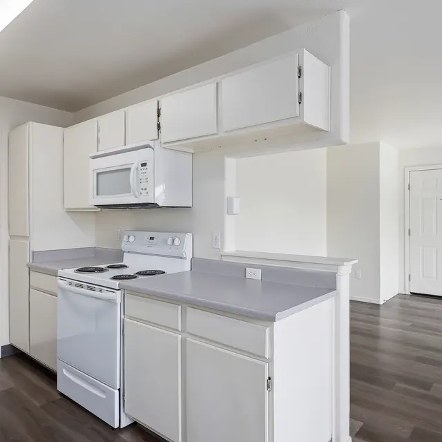 Contemporary Kitchen Design A modern kitchen with white cabinetry, gray countertops, and appliances including a stove and microwave. The kitchen opens into a spacious area with a door visible in the background.