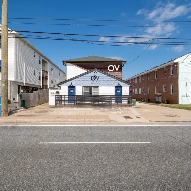 A view of a building with a sign that reads 'OV', surrounded by other residential structures and a clear blue sky.