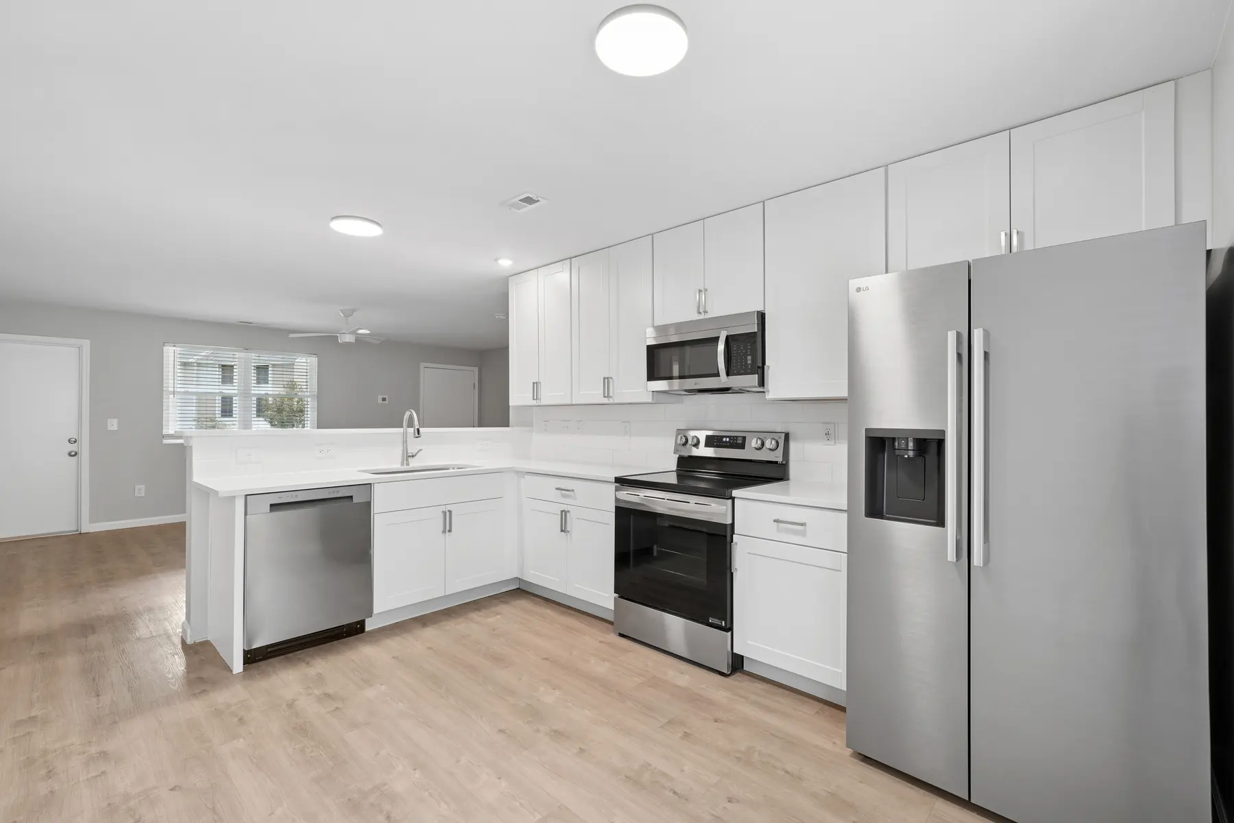 A modern kitchen with white cabinetry, stainless steel appliances, and a spacious layout featuring a central island and hardwood floors.