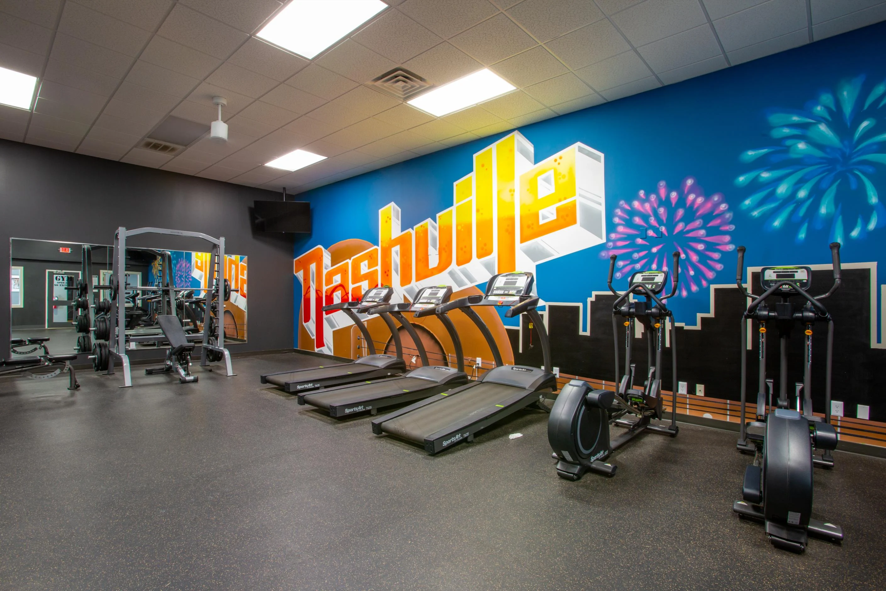 Interior of a modern gym featuring exercise equipment and a colorful mural with the word 'Nashville'.