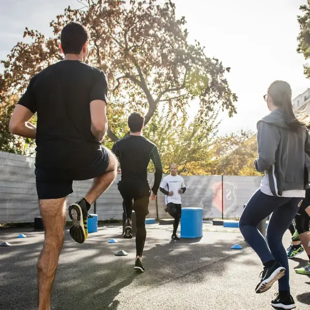 Outdoor Group Training Session A group of men participating in an outdoor training session, jogging and engaging in exercises on a paved track with colorful cones and equipment around them.