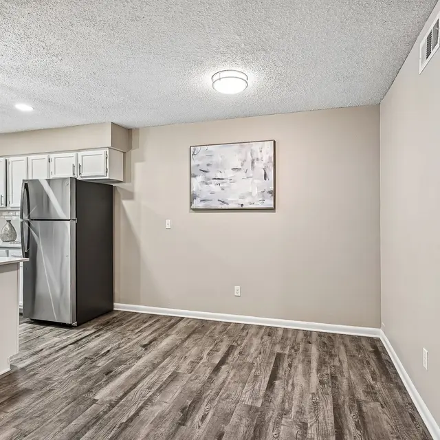 Stylish Kitchen and Living Space A modern kitchen and living area featuring a stainless steel refrigerator and white cabinets. The room has a light wood floor and a piece of abstract art on the wall.