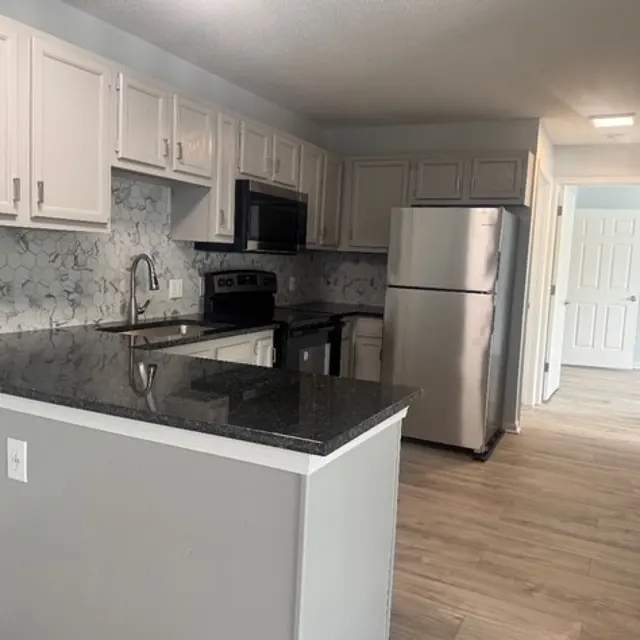 Modern kitchen featuring light cabinets, black countertops, and stainless steel appliances.