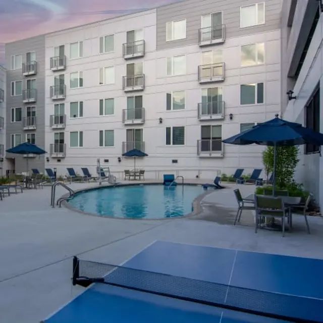A well-maintained hotel pool area featuring a circular swimming pool surrounded by lounge chairs and umbrellas.