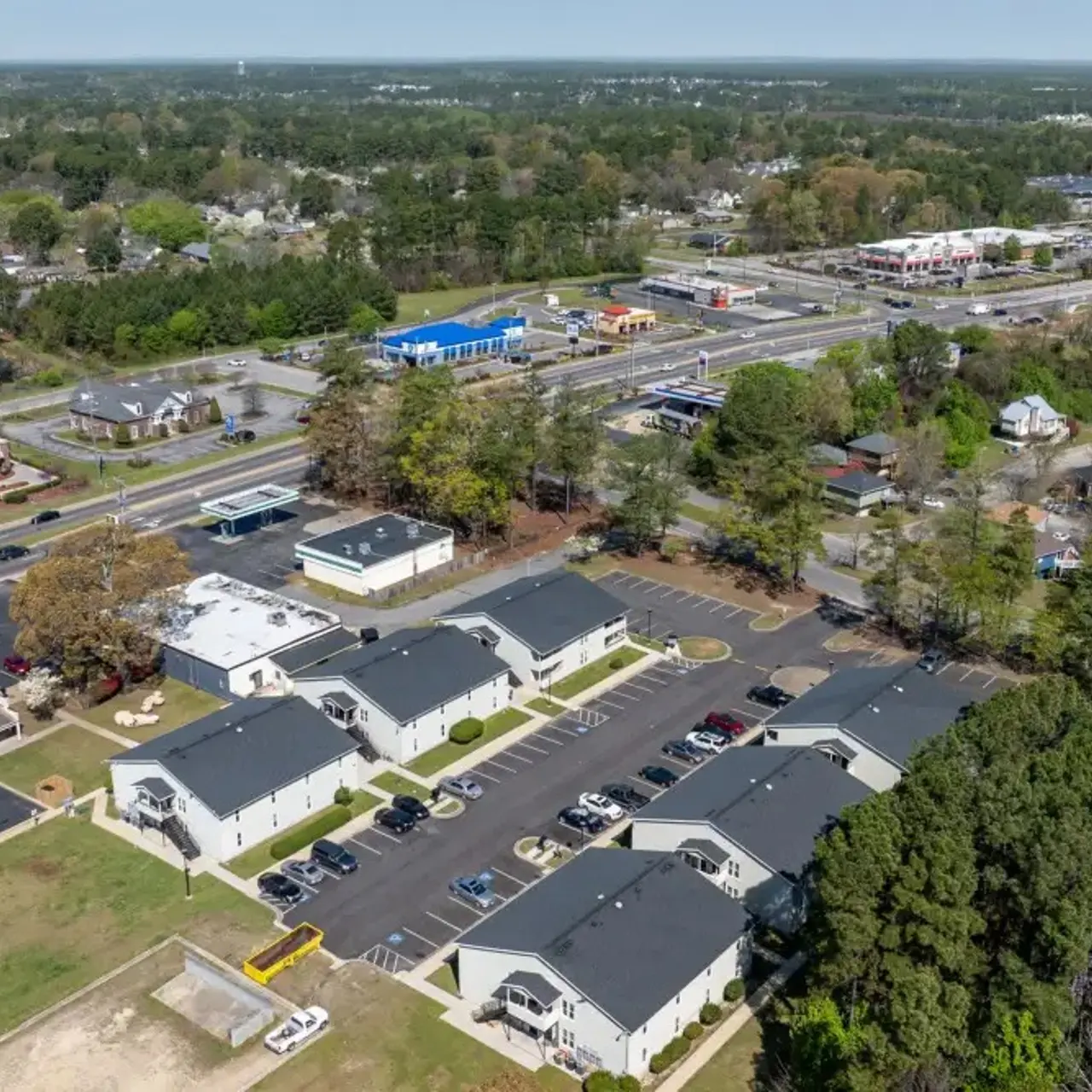 Aerial view of a suburban area featuring residential buildings, a parking lot, and roads running through the landscape.