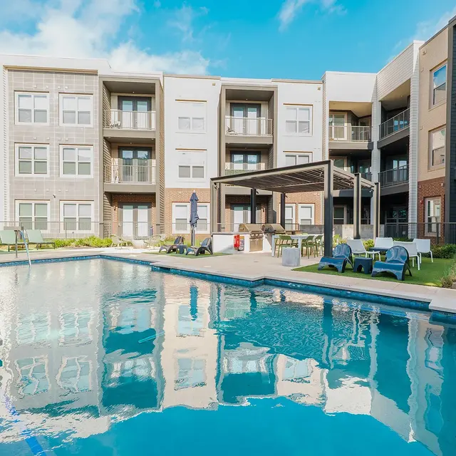 A tranquil pool area surrounded by modern apartment buildings, featuring lounge chairs and a pergola.