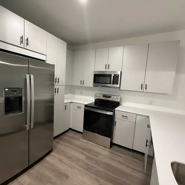 A modern kitchen featuring stainless steel appliances, including a refrigerator, oven, and microwave, with sleek white cabinetry and light wood flooring.