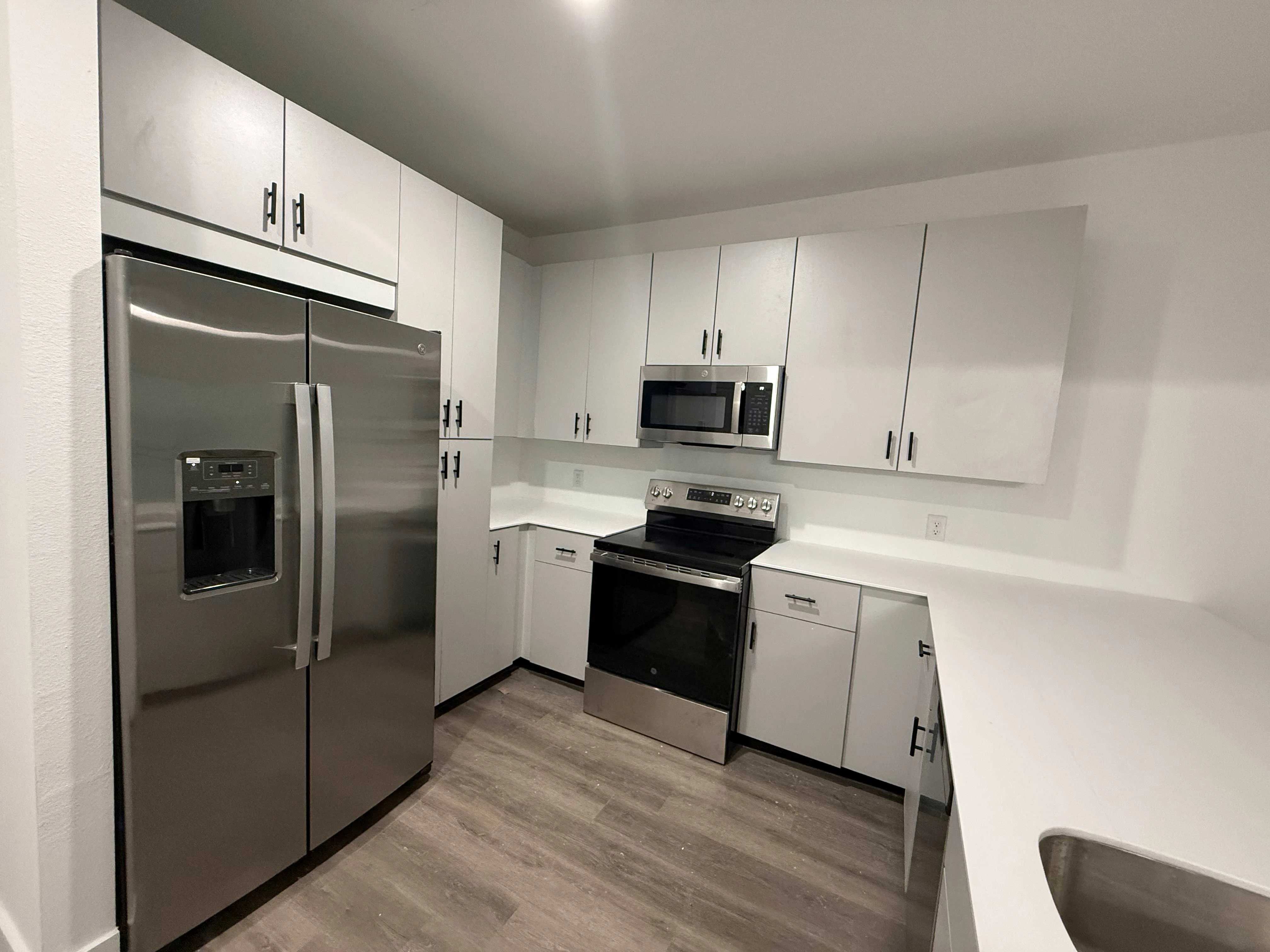 Modern Kitchen Design A modern kitchen featuring stainless steel appliances, including a refrigerator, oven, and microwave, with sleek white cabinetry and light wood flooring.