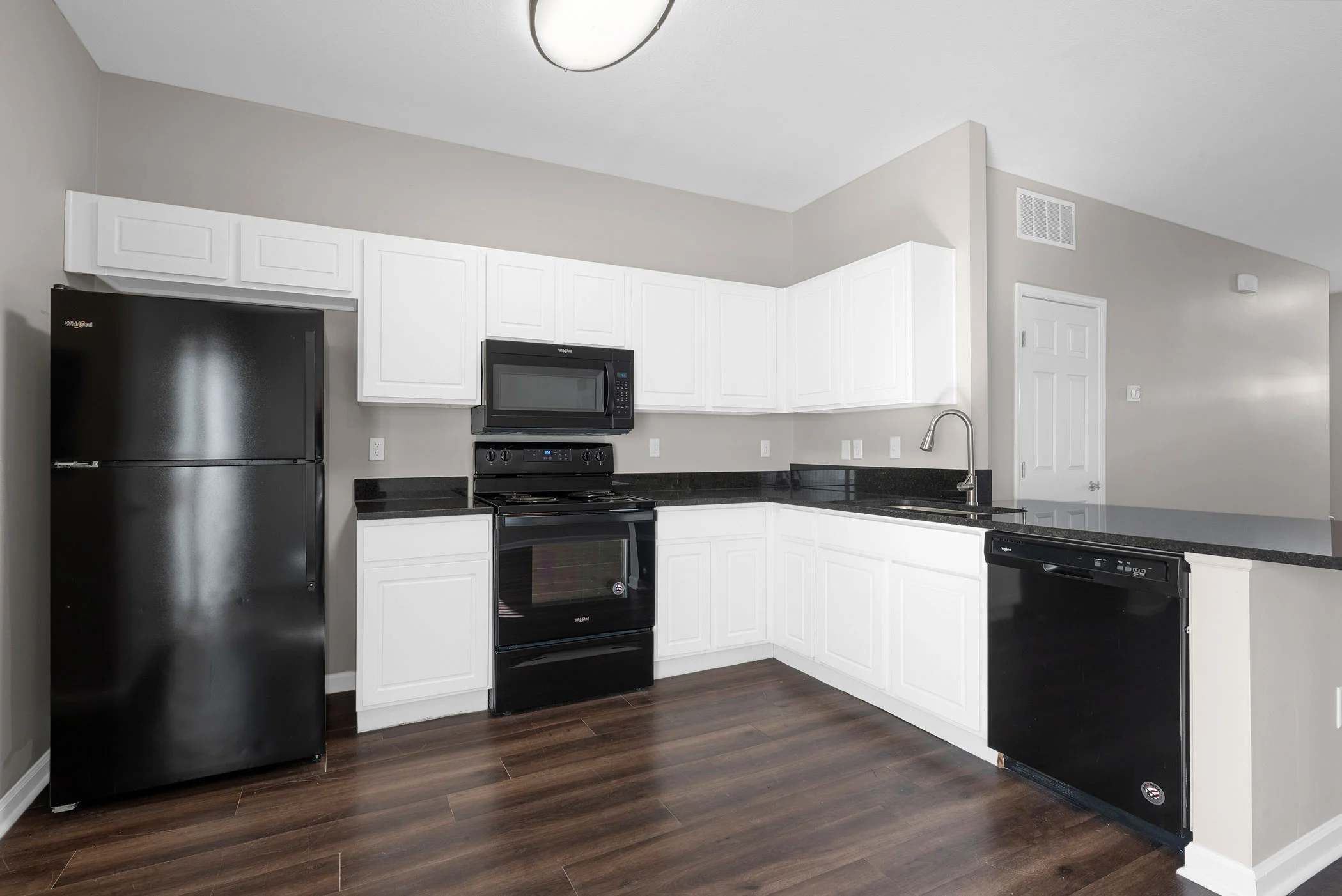 A modern kitchen featuring black appliances, white cabinets, and dark wood flooring.