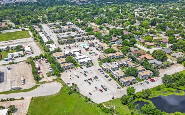 Aerial view of a shopping area surrounded by trees and homes, with parking lots and a small body of water nearby.