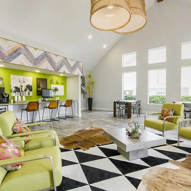 The Edge Apartments Spacious resident clubhouse with breakfast bar, two tables and chairs, and lime green features and four cushioned chairs in a well lit room