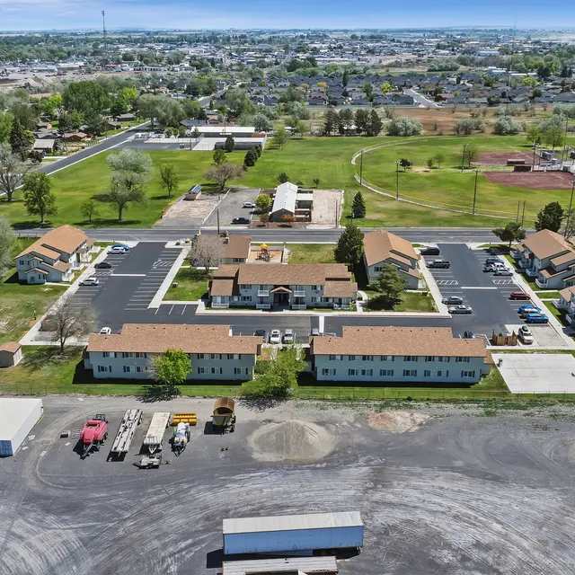 Aerial View of Community Complex Aerial view of a community complex with several buildings, parking areas, and a green park-like space in the background.