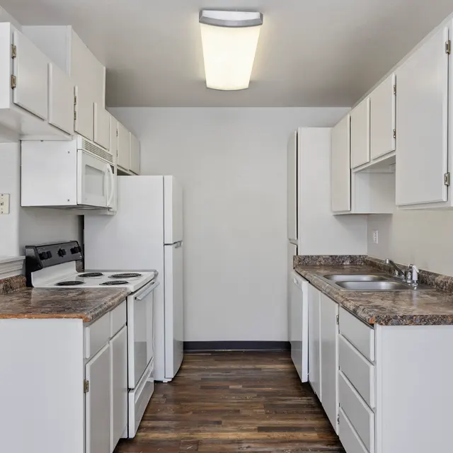 Modern Kitchen Interior A modern kitchen featuring white cabinets, a stove, refrigerator, and sink. The countertops are dark with a wooden look, and the floor is also wood-like. The walls are painted light and the overall appearance is clean and organized.