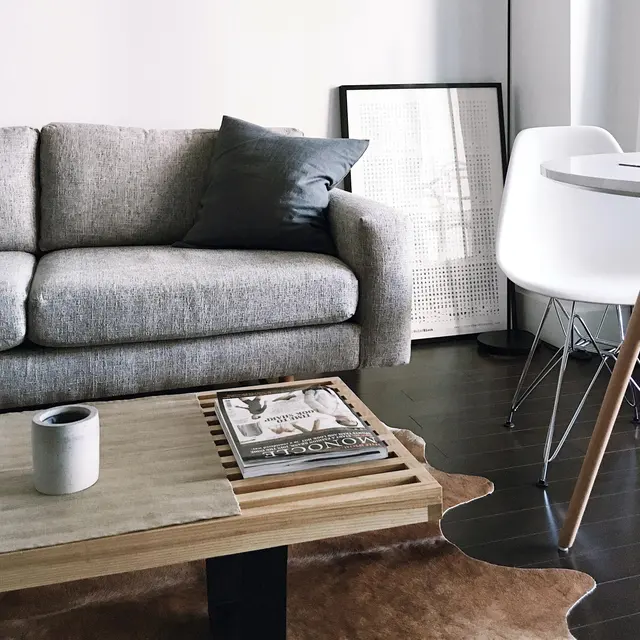 Modern living room with a gray sofa, a wooden coffee table, magazines, and a dining area featuring a white chair and patterned decor.