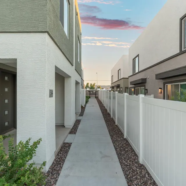 Pathway Between Modern Townhomes A narrow walkway between modern townhomes, lined with white fences and small shrubs.