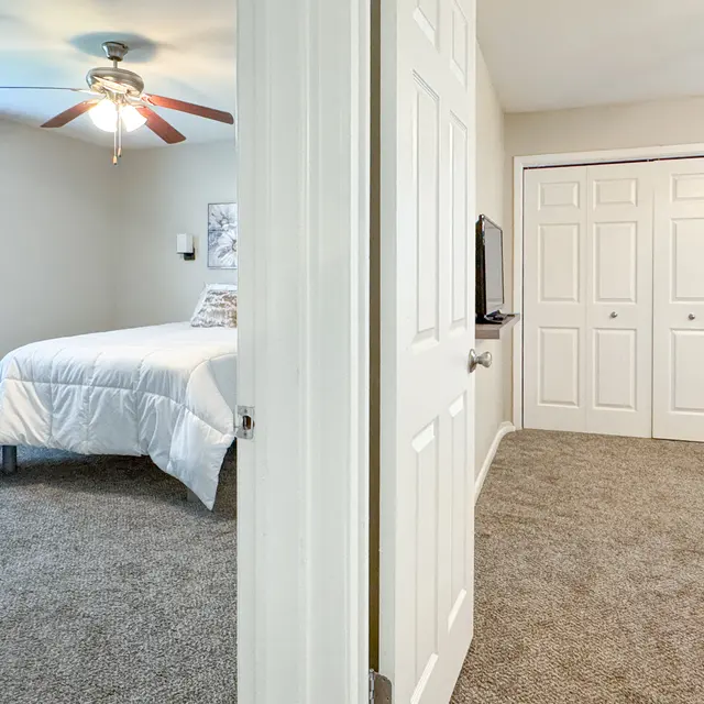 A view of a bright and cozy bedroom with a light-colored bedspread and blue curtains, showing an open door leading to a closet area.