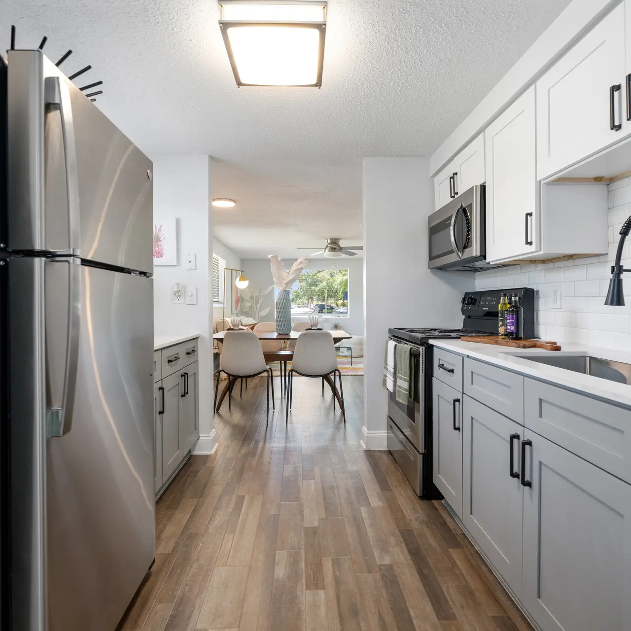 A modern kitchen with stainless steel appliances, wooden flooring, and a view into a dining area with a table and chairs.