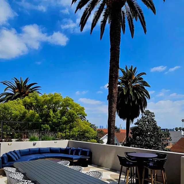 Stunning Outdoor Patio with Palm Trees A serene outdoor patio with a geometric patterned floor, featuring stylish lounge furniture, a dark table, and palm trees against a bright blue sky with scattered clouds.