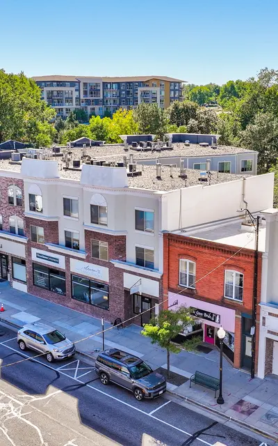 An aerial view of a modern urban street lined with various shops and trees on both sides, with a clear blue sky above.
