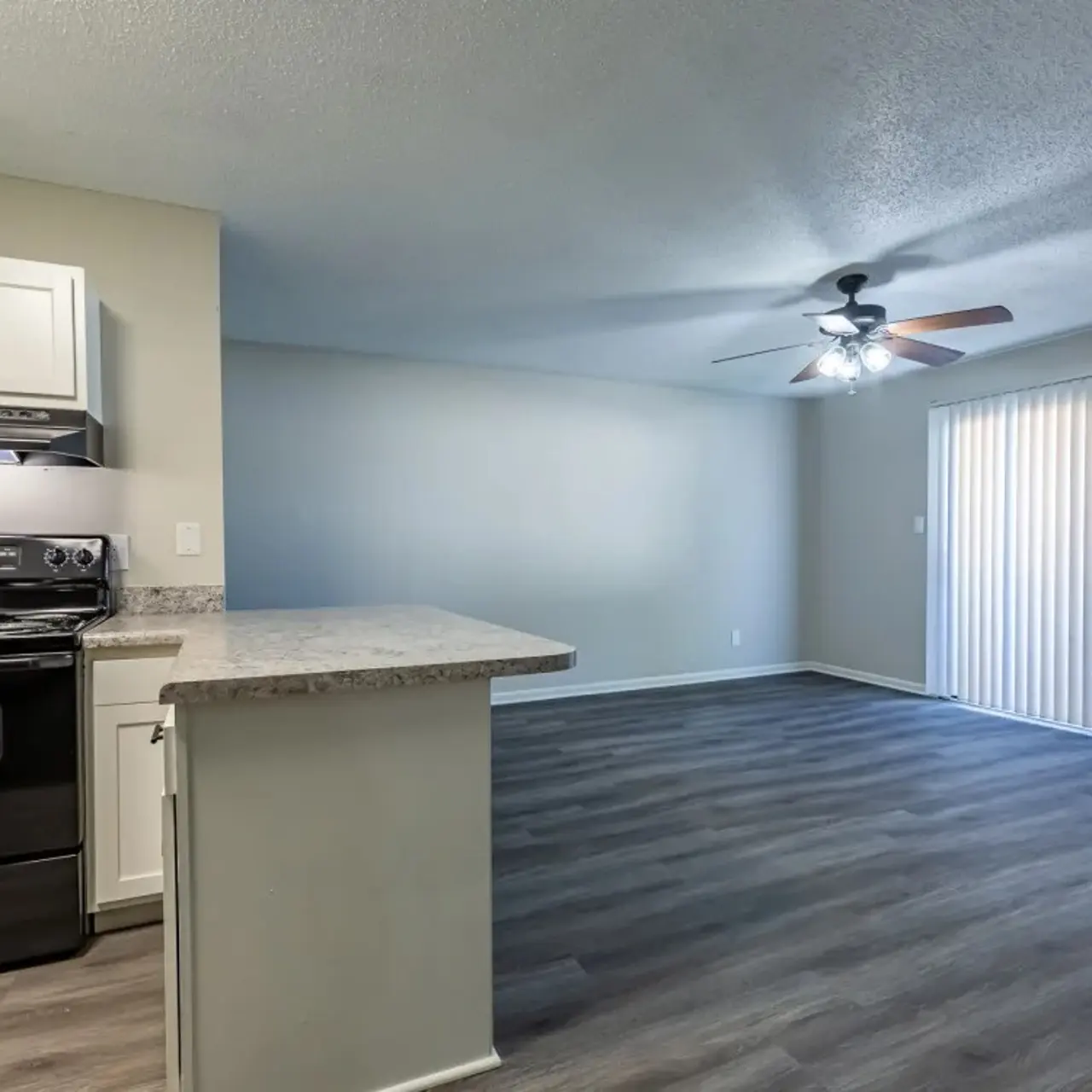 Interior view of a modern kitchen and living room area featuring a black stove, light-colored cabinets, and laminate flooring.
