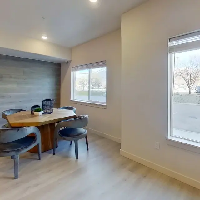 A modern dining area featuring a wooden table surrounded by gray chairs, with a large window letting in natural light and a view of trees outside.