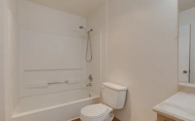 A clean and simple bathroom featuring a bathtub with a showerhead, a modern toilet, and a vanity with a sink.