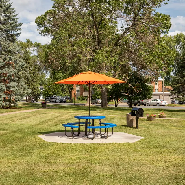 Regency Park - A colorful picnic table with an orange umbrella in a park surrounded by grass and trees.