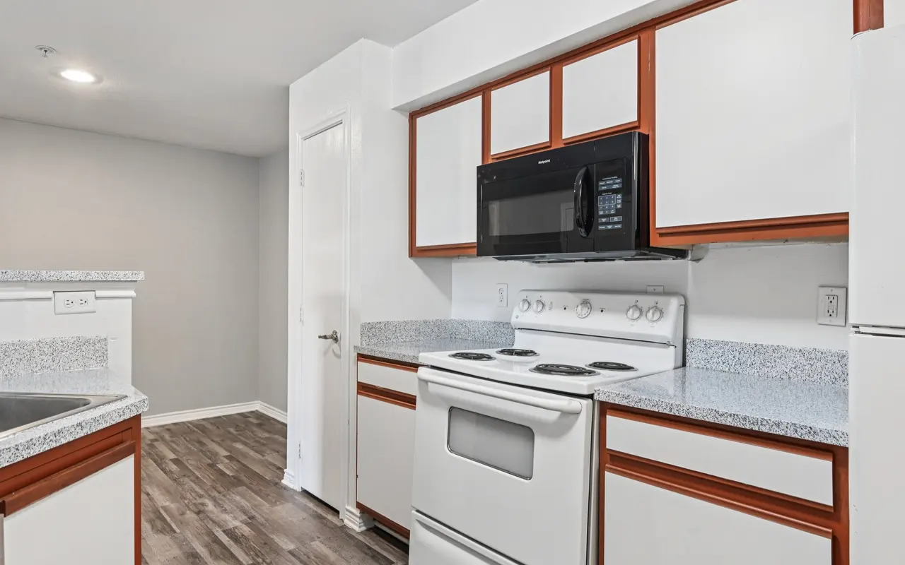 Modern kitchen with white cabinets and dark wood accents, featuring a stove, microwave, and granite countertops.