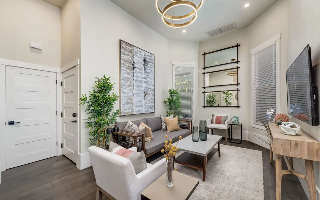 A modern living room with light walls, a gray sofa, and decorative plants; features stylish decor including shelves and art.