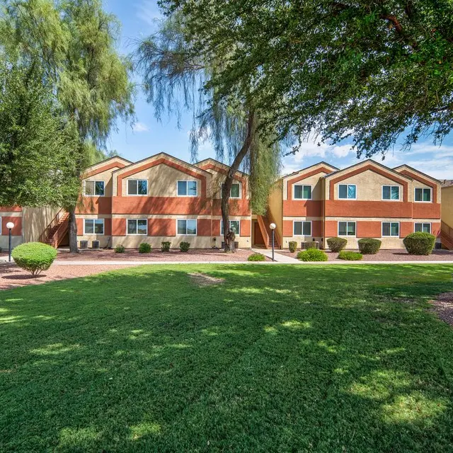 A colorful apartment complex surrounded by well-maintained lawns and trees under a clear blue sky.