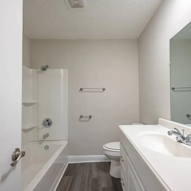 A clean and simple bathroom featuring a white bathtub with a shower, a white vanity with a sink, a large mirror, and light gray walls.