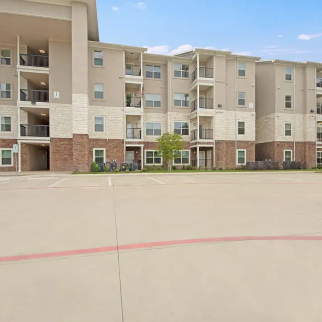 Modern Apartment Complex A modern three-story apartment building with light-colored siding and brick accents, surrounded by a parking lot and a few trees.